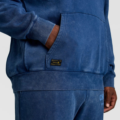 A blue Mineral Wash Pullover Hoodie, C Patch Logo by Champion, featuring a kangaroo pocket and a small rectangular logo patch above the hem.