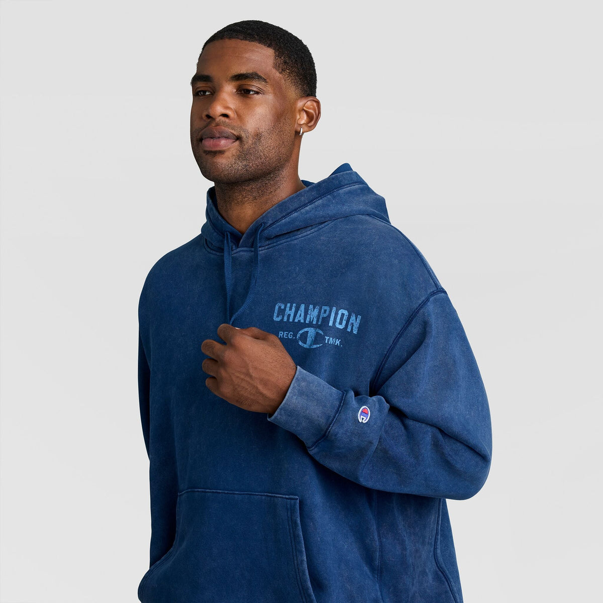 A man wearing a blue Mineral Wash Pullover Hoodie, C Patch Logo, featuring a faded chest logo and a small sleeve patch.