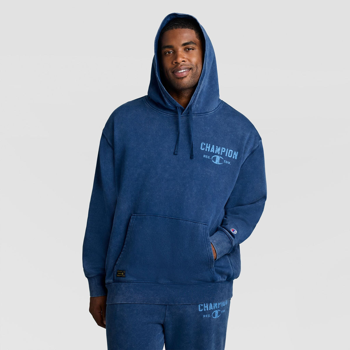 A man wearing a vintage blue Mineral Wash Pullover Hoodie, C Patch Logo with a faded logo on the chest.