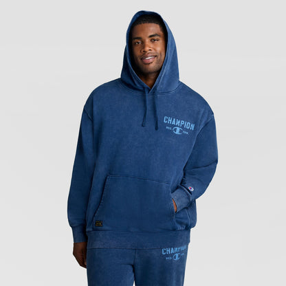A man wearing a vintage blue Mineral Wash Pullover Hoodie, C Patch Logo with a faded logo on the chest.
