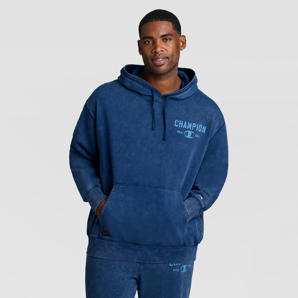 A man wears a blue Mineral Wash Pullover Hoodie, C Patch Logo, featuring a logo printed on the chest.
