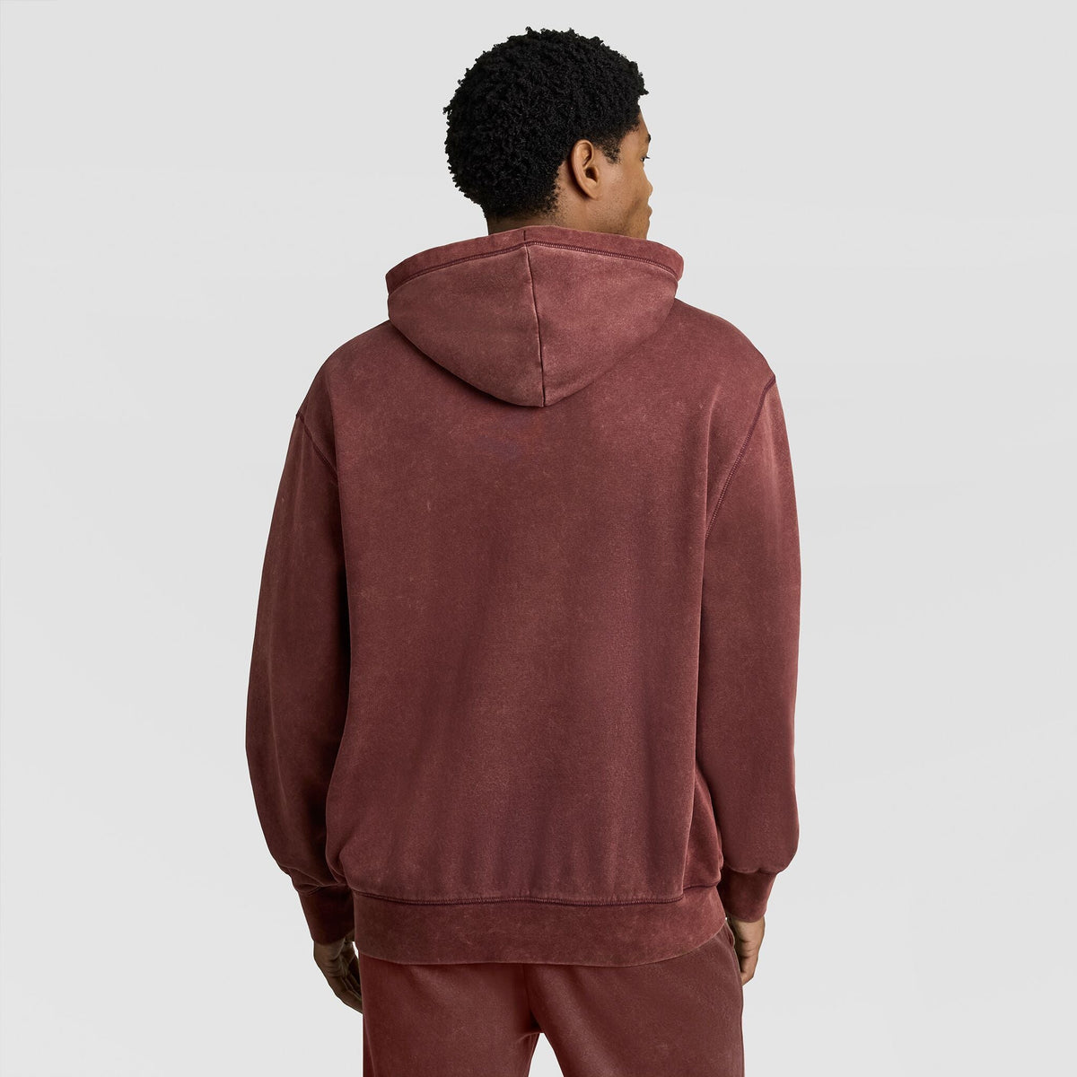 A person viewed from behind, wearing a faded, dark red Champion Mineral Wash Pullover Hoodie, C Patch Logo.