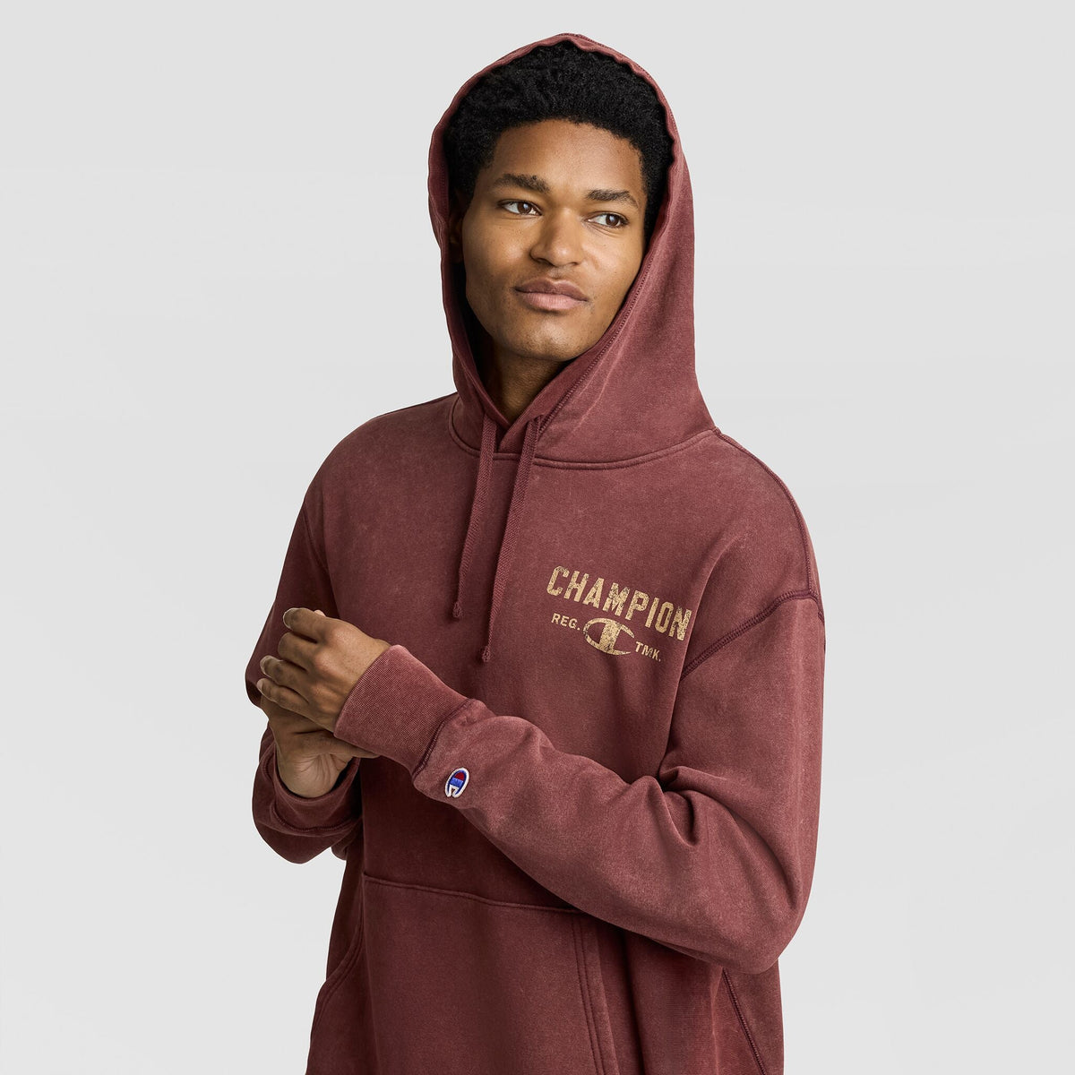 A man wearing a burgundy vintage Mineral Wash Pullover Hoodie, C Patch Logo with a distressed-look logo on the chest and a small patch on the sleeve.