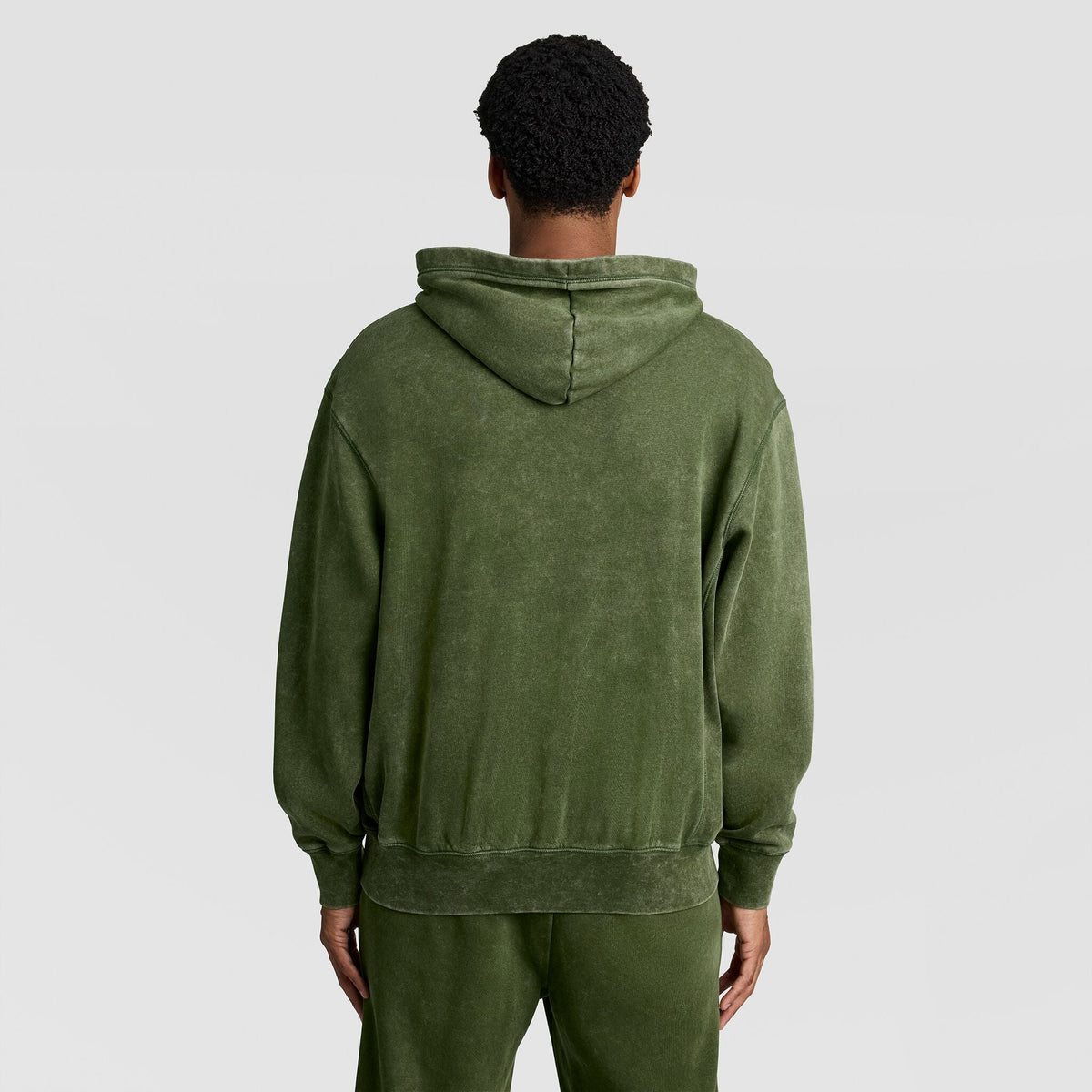 A person viewed from behind wearing a mottled olive green Mineral Wash Pullover Hoodie, C Patch Logo by Champion.