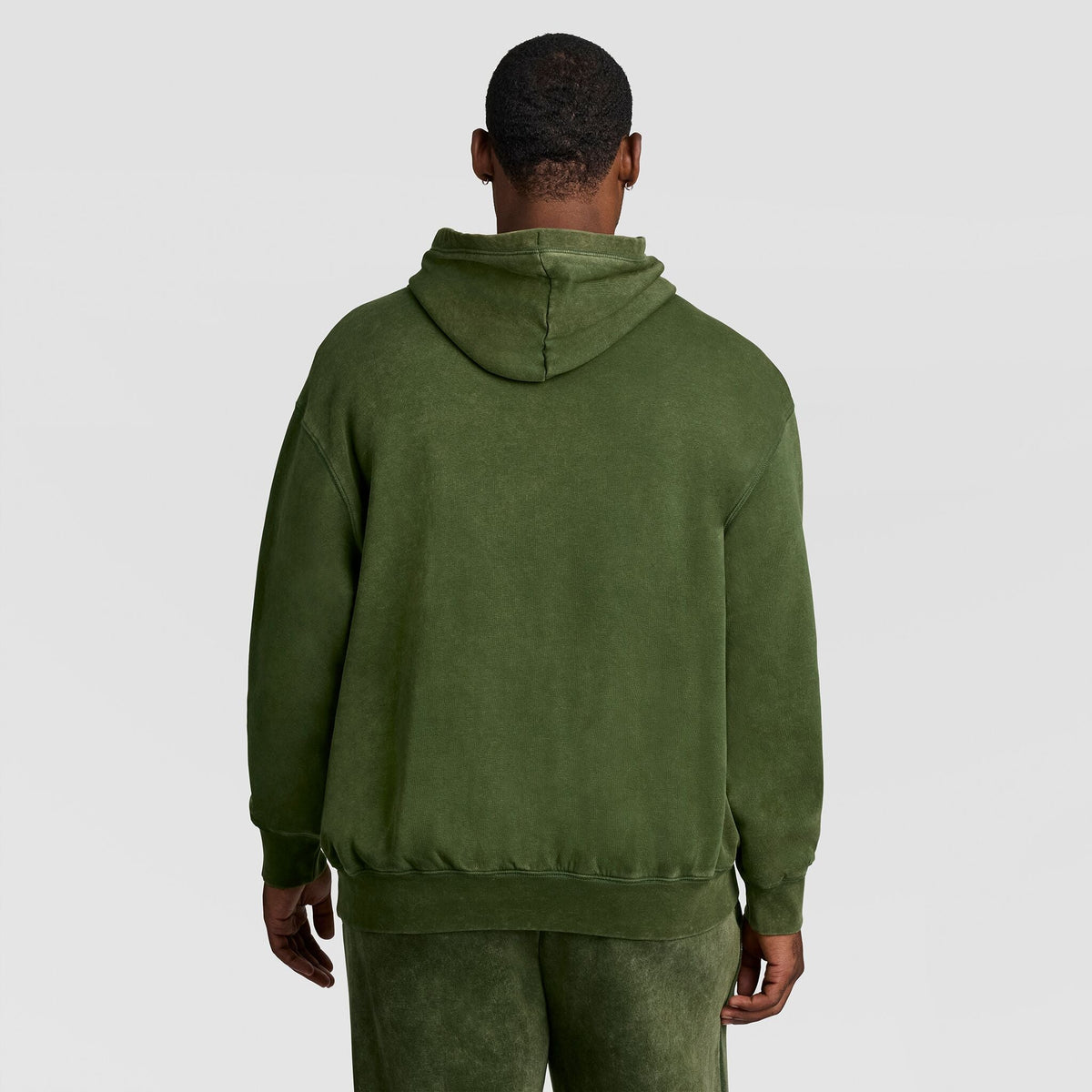 A person seen from behind wearing an olive green Mineral Wash Pullover Hoodie, C Patch Logo by Champion.
