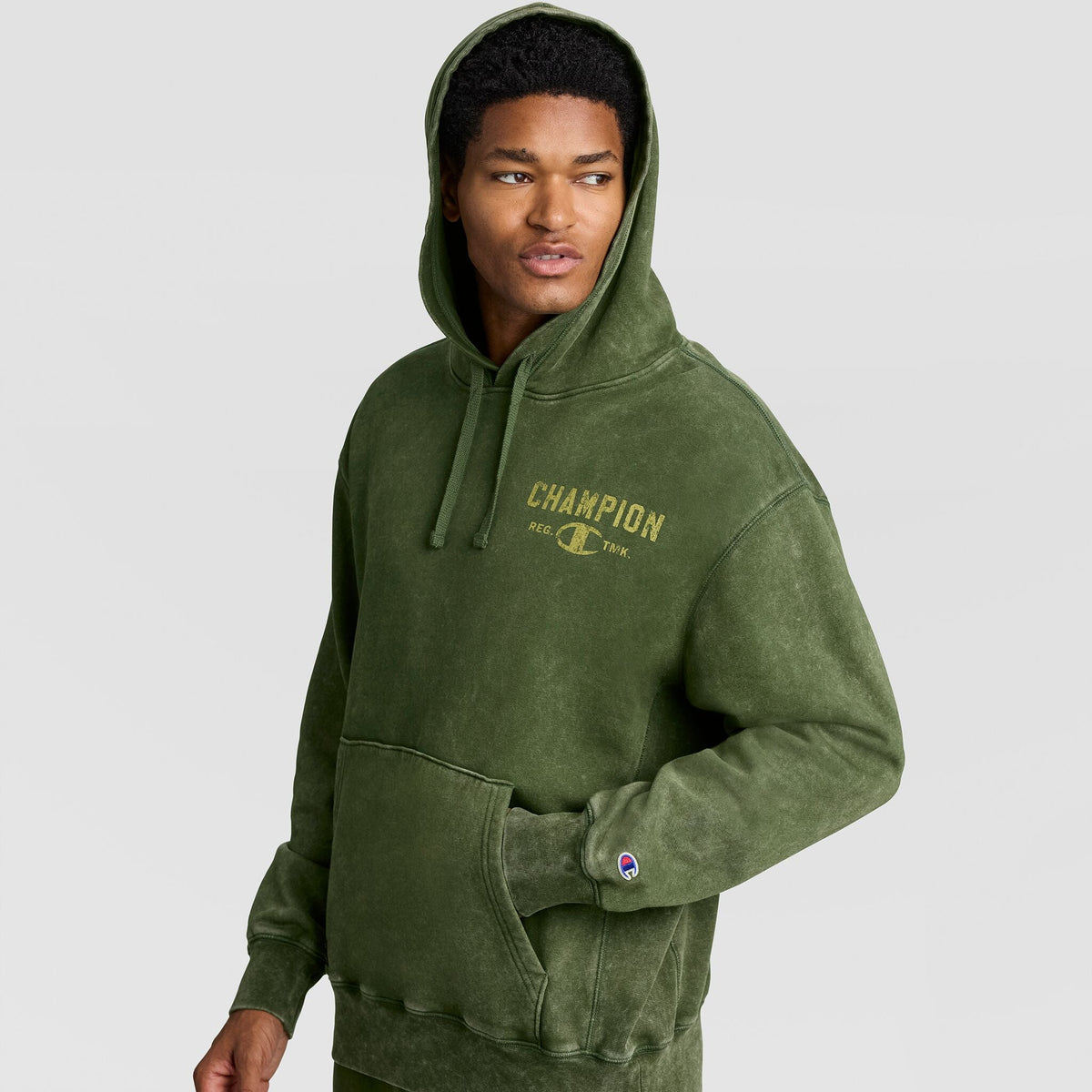 A person wearing a green Mineral Wash Pullover Hoodie, C Patch Logo with a graphic on the chest and a small patch on the sleeve.