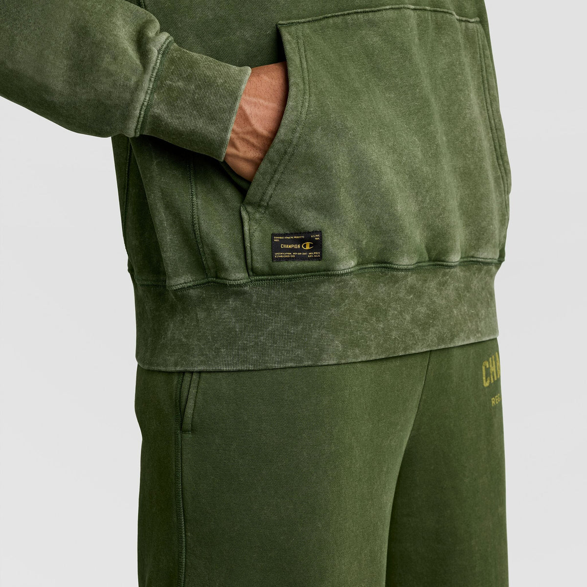 Olive green Mineral Wash Pullover Hoodie, C Patch Logo featuring a hand in the front pocket and a small rectangular logo patch near the hem.