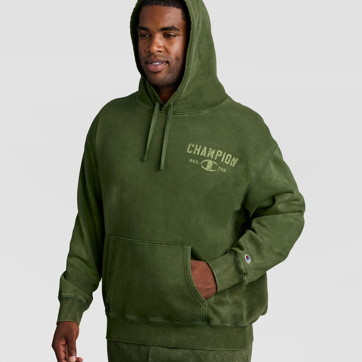 A man wears a vintage Mineral Wash Pullover Hoodie, C Patch Logo featuring a faded graphic logo on the chest and a small patch on the sleeve.