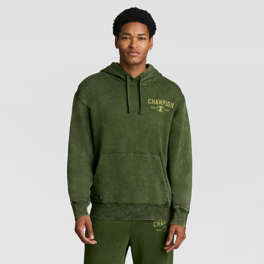 A person wears a vintage olive green Champion Mineral Wash Pullover Hoodie, C Patch Logo, featuring a hood, drawstrings, front pocket, and a chest graphic.