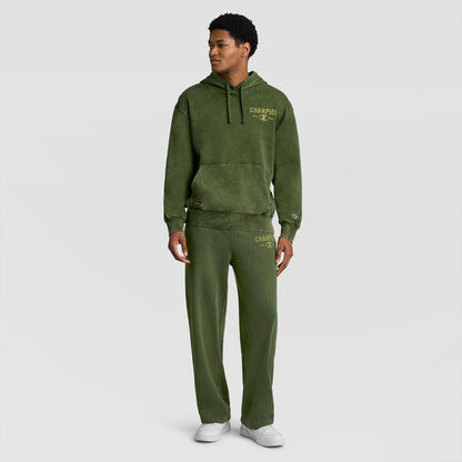 A man wearing a green vintage Mineral Wash Pullover Hoodie, C Patch Logo and matching sweatpants with a logo on the chest.