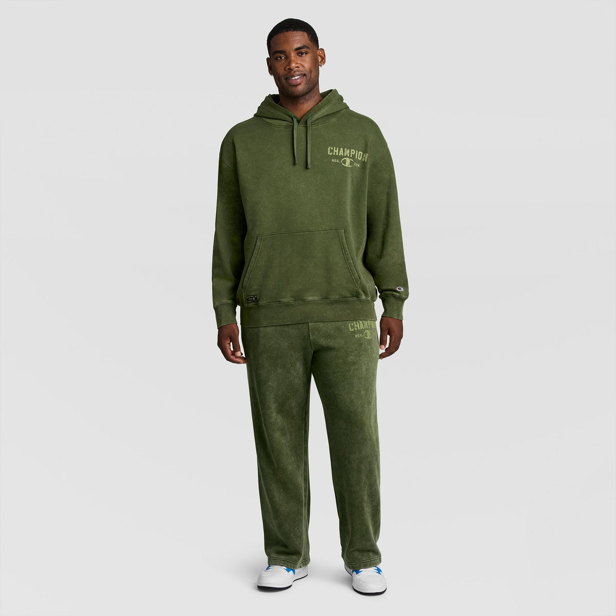 A man wearing a mineral wash Mineral Wash Pullover Hoodie, C Patch Logo and matching sweatpants, both featuring logo text on the chest and thigh.