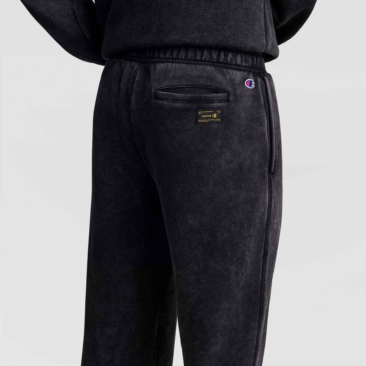 Back view of dark grey Mineral Wash Open Hem Pant featuring a back pocket, a rectangular Champion brand label, and a small logo embroidered near the waist.