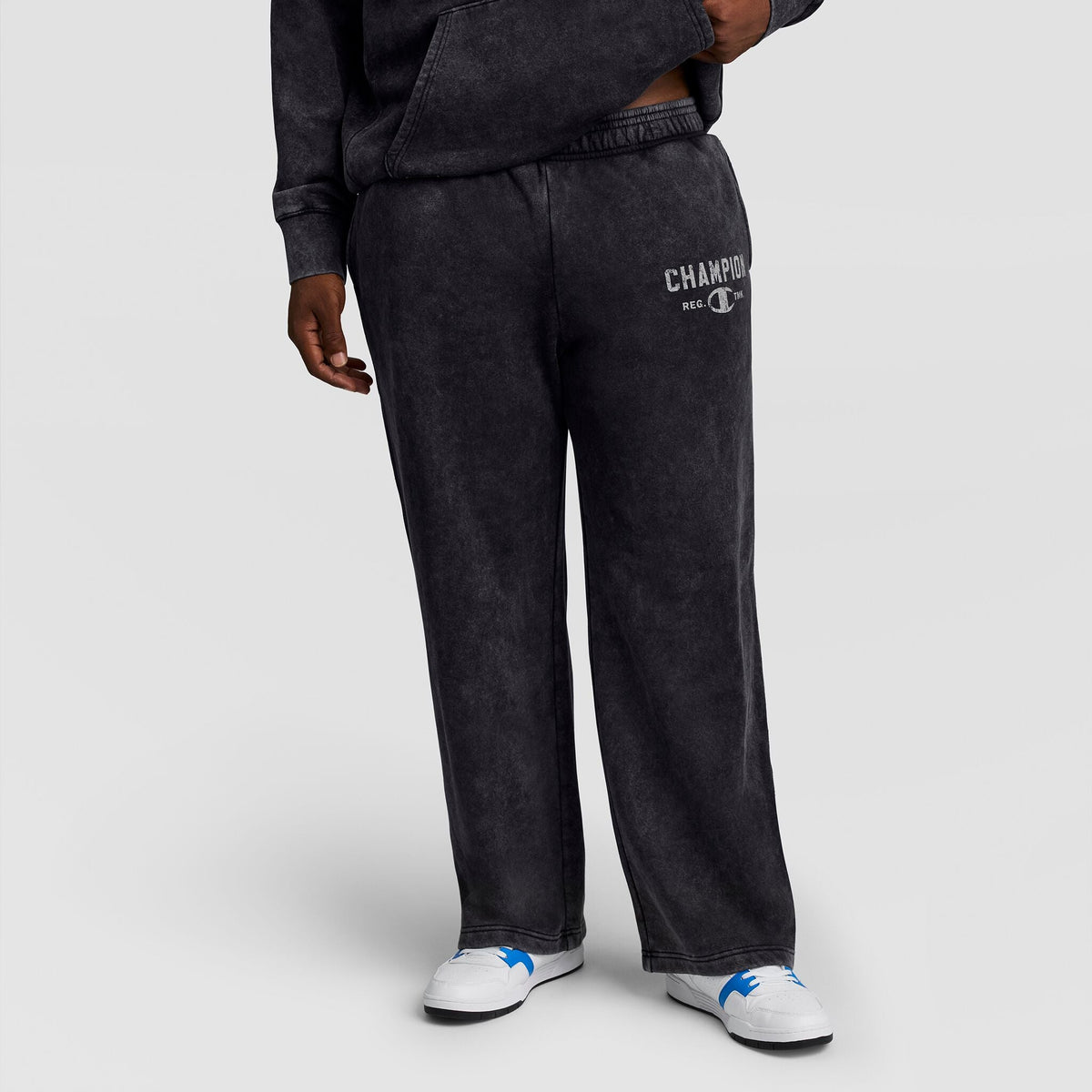 A person wears black Mineral Wash Open Hem Pant by Champion, featuring an open hem and a logo on the left hip.