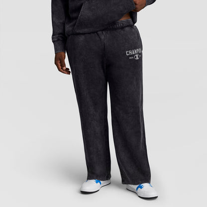 A person wears black Mineral Wash Open Hem Pant by Champion, featuring an open hem and a logo on the left hip.