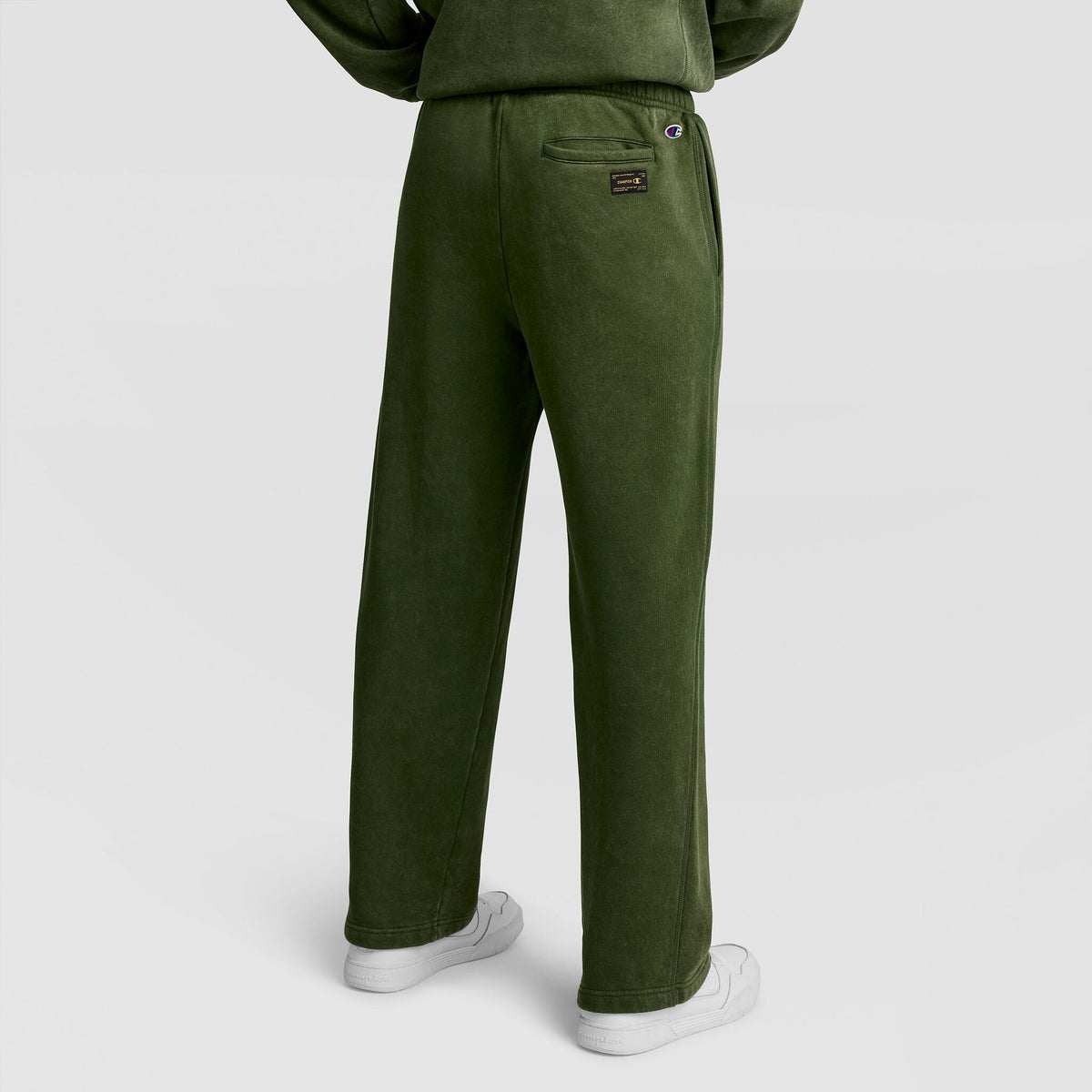 A person viewed from behind wearing olive green Mineral Wash Open Hem Pant by Champion and white sneakers.