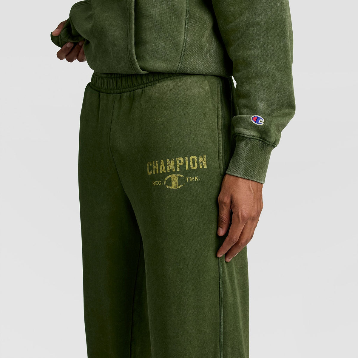 Mineral Wash Open Hem Pant in olive green athletic fleece with an open hem and a distressed gold Champion logo on the thigh for a vintage look.