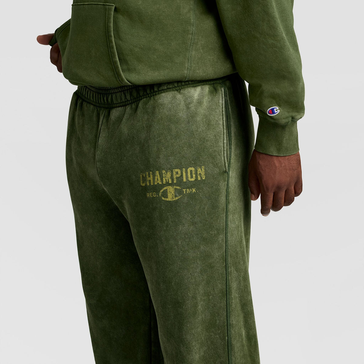 Champion Mineral Wash Open Hem Pant in olive green athletic fleece with an open hem and a faded logo printed on the thigh.