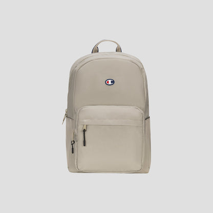 Level Backpack by Champion in beige, featuring a front zipper pocket, small top handle, and the Champion logo in blue, red, and white centered on the upper front. Designed for everyday carry, this backpack includes a padded laptop sleeve for added convenience. Set against a light gray background.