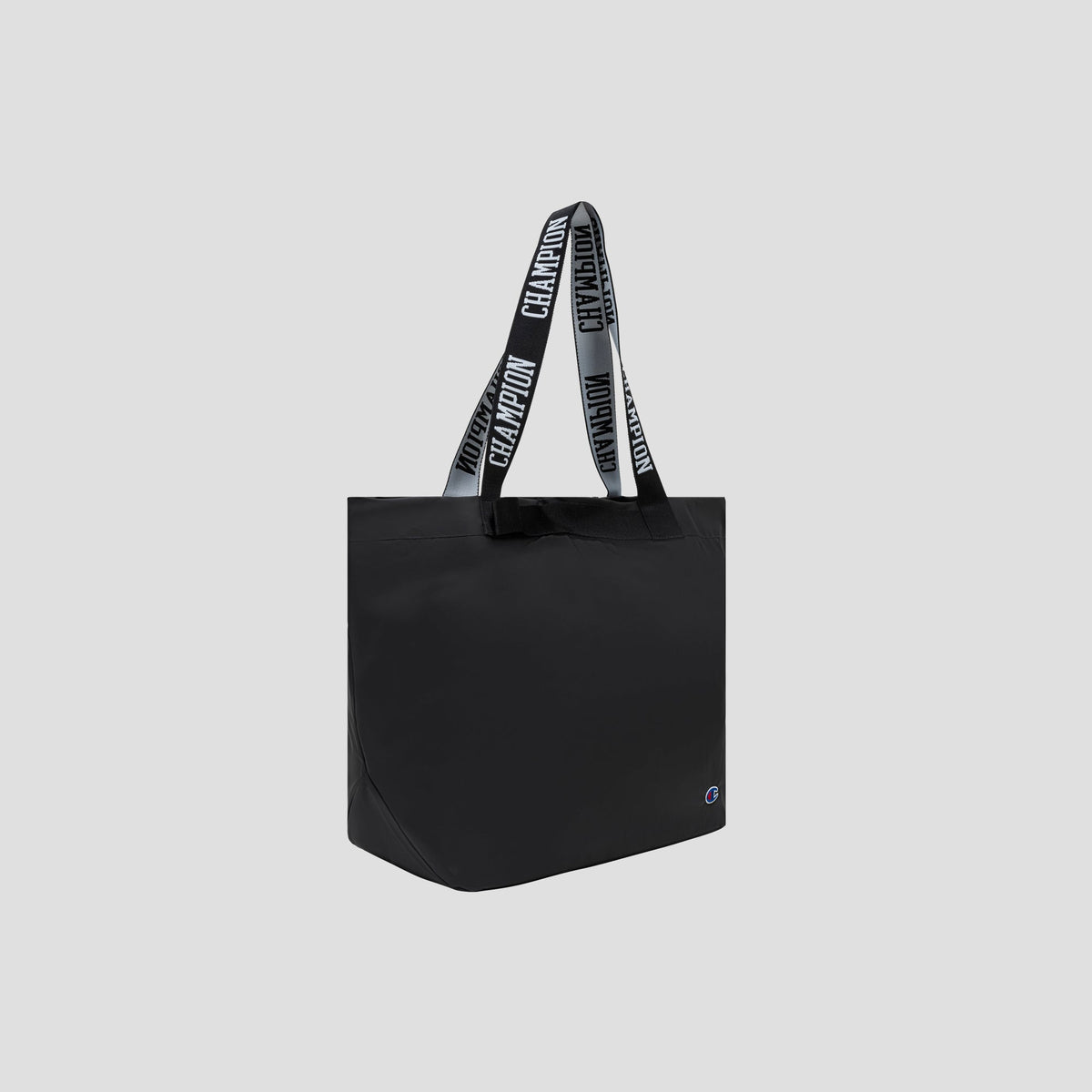 The Miller Coated Shopper Tote by Champion is a spacious black bag with two handles, featuring bold white “CHAMPION” lettering. This weather-resistant tote also includes a small Champion logo on the lower right corner and is displayed against a plain gray background.