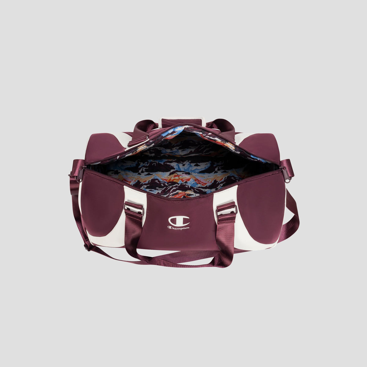 A maroon and white Oracle Duffel Bag by Champion, featuring handles and a shoulder strap, sits open to reveal its colorful, patterned interior lining. The stylish sports bag displays the Champion logo on the front pocket.
