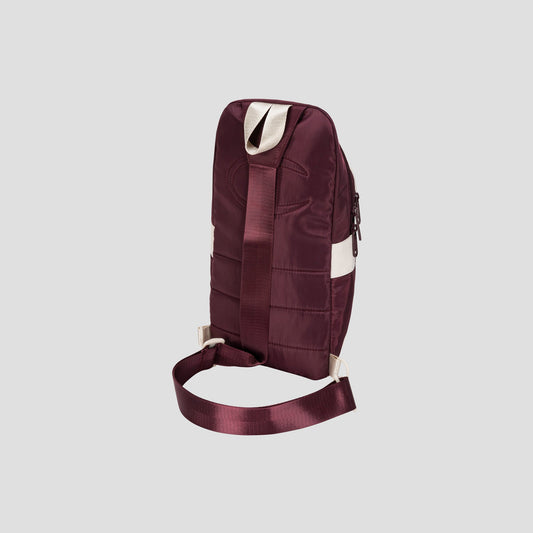A maroon Oracle Sling Pack by Champion, featuring a single adjustable strap, white accent, and quilted fabric, displayed on a light gray background.