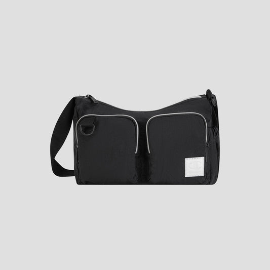 The Champion Quartz Small Messenger Bag, crafted from lightweight black nylon, features two front zippered pockets, a white rectangular patch, and an adjustable strap. It is photographed against a plain light gray background.