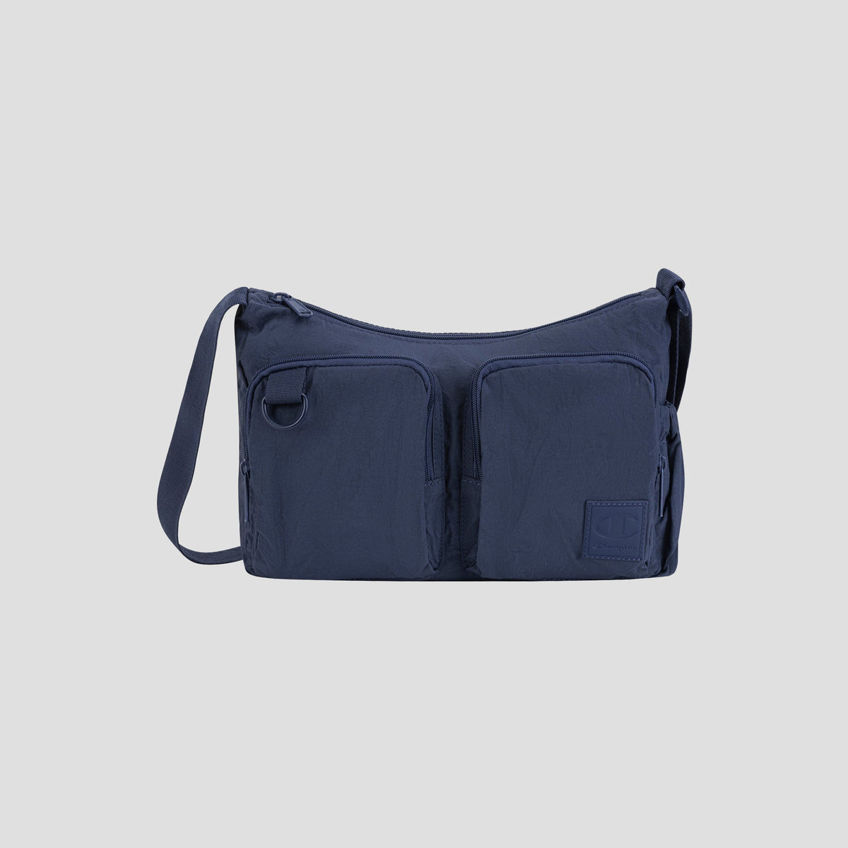 The Champion Quartz Small Messenger Bag, crafted from lightweight navy blue nylon, features two front zippered pockets, an adjustable shoulder strap, and a small square logo patch on the lower right corner. Displayed against a light gray background, this versatile messenger bag is perfect for everyday adventures and travel.