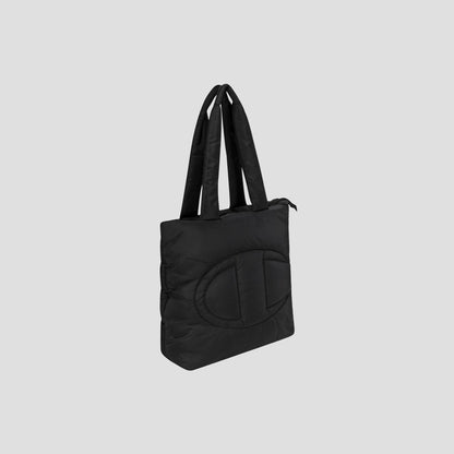 The Champion Quilted Billie Tote features a black quilted design with two long handles and a subtle, large oval pattern stitched on the front, shown against a plain light gray background—perfect for everyday use.