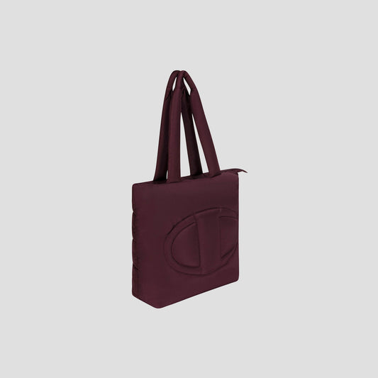 The Champion Quilted Billie Tote is a maroon rectangular bag with double handles and a large embossed oval logo on the front, ideal for everyday use, showcased against a plain light gray background.