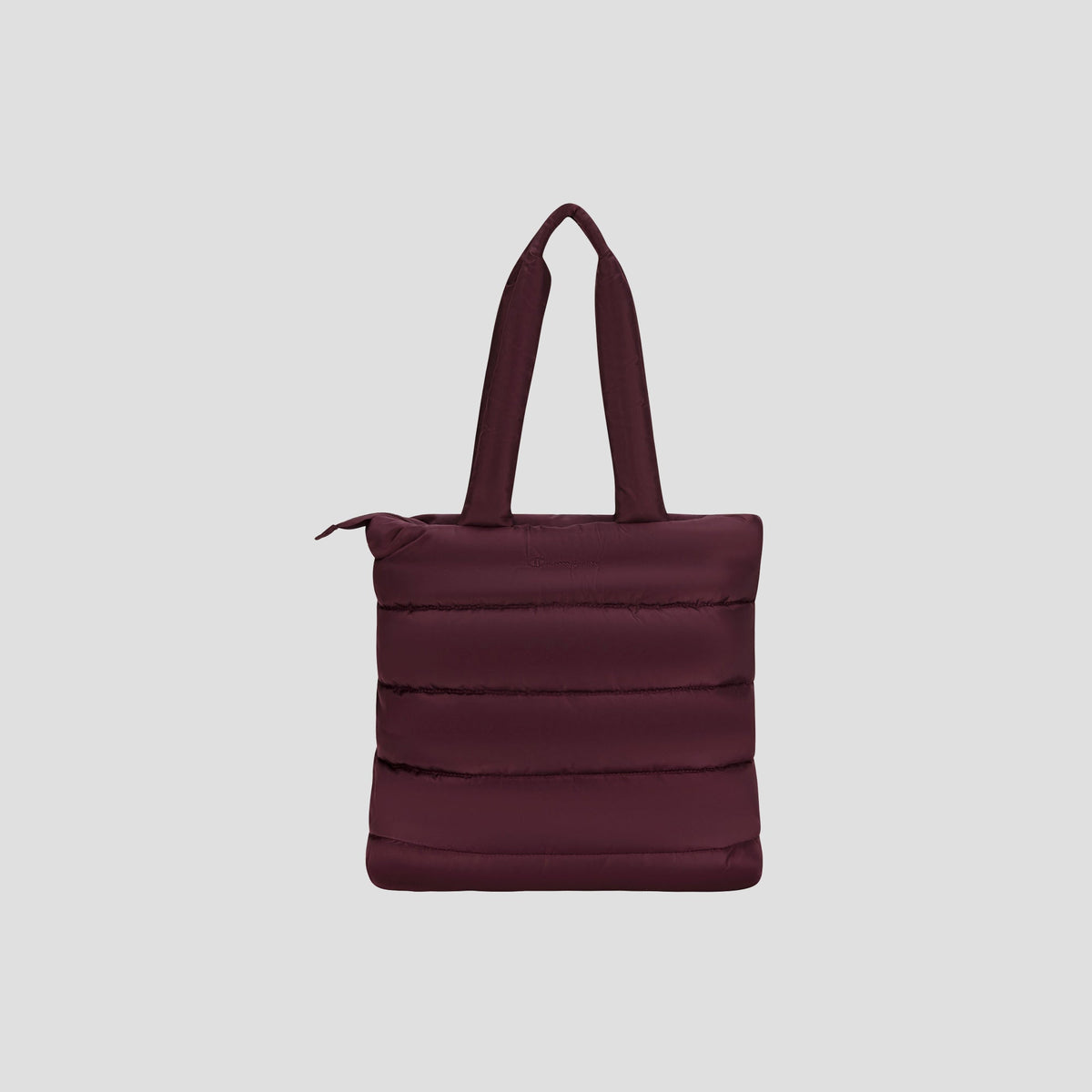 The Champion Quilted Billie Tote is a stylish, dark maroon tote bag featuring padded handles, vertical quilted stitching, and a secure zipper closure—perfect for everyday use. It is displayed against a plain light gray background.