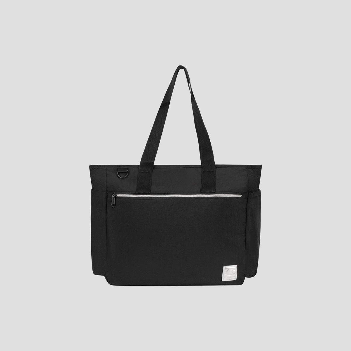 The Champion Quartz East West Tote is a black crinkle nylon bag featuring two shoulder straps, a spacious front zip pocket, side pockets, and a small white label at the bottom right corner. It also includes a padded laptop sleeve and is displayed against a plain light gray background.
