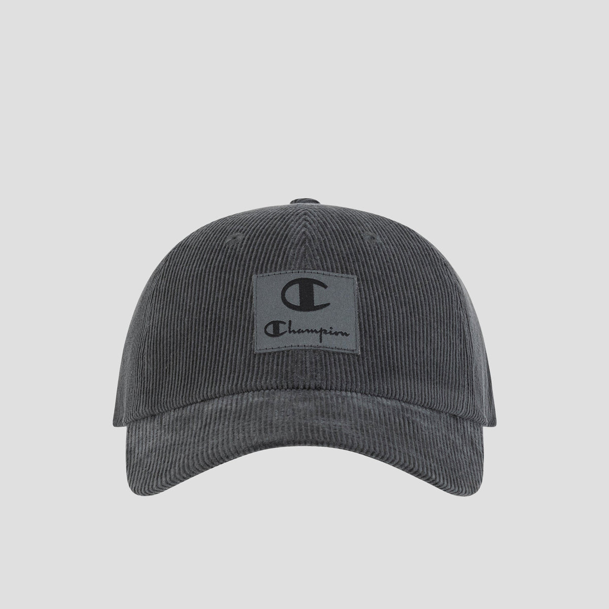 Introducing the Ridge Corduroy Adjustable Cap by Champion—a dark grey vintage-inspired baseball cap crafted from corduroy. Featuring a relaxed fit, curved brim, and an adjustable back closure for custom comfort, this cap showcases a rectangular front patch with the iconic Champion logo and text. Photographed on a plain white background.