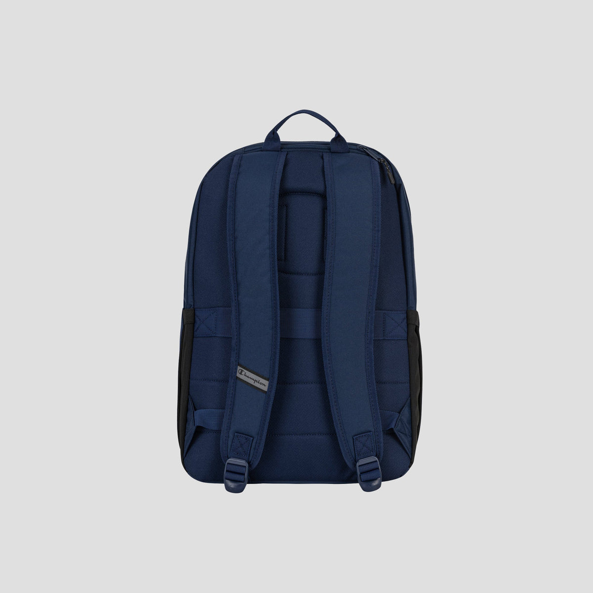 The System Backpack by Champion is displayed from the back against a plain light gray background, showcasing its navy blue color, padded shoulder straps, top carry handle, and multiple storage compartments—including a padded laptop sleeve.