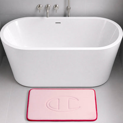 A modern white bathtub with a light pink Champion Quilted Logo Memory Foam Bath Mat, featuring an embossed circular design, placed on a light gray tiled bathroom floor.