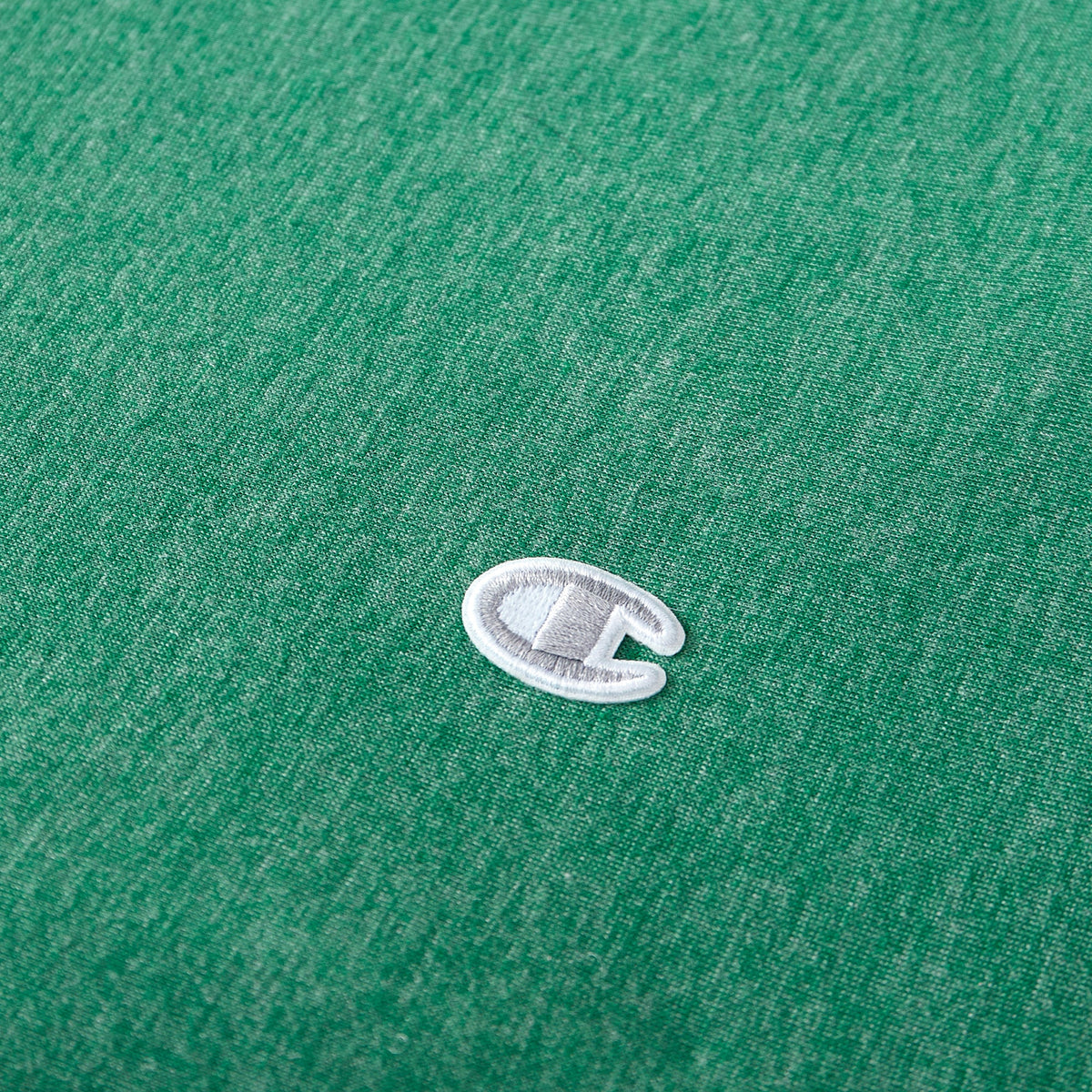 A close-up of a small, white and gray embroidered Champion C logo on green fabric—reminiscent of the signature detailing found on Champion’s Reversible Solid Jersey Comforter Sets.