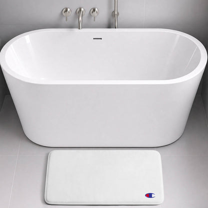A modern white freestanding bathtub with a wall-mounted faucet sits on gray tile. In front of the tub is the Champion Logo Patch Memory Foam Bath Mat—a white, rectangular bath mat crafted from memory foam for extra comfort and designed to be skid-resistant. A small blue and red Champion logo patch adds a subtle yet stylish touch.