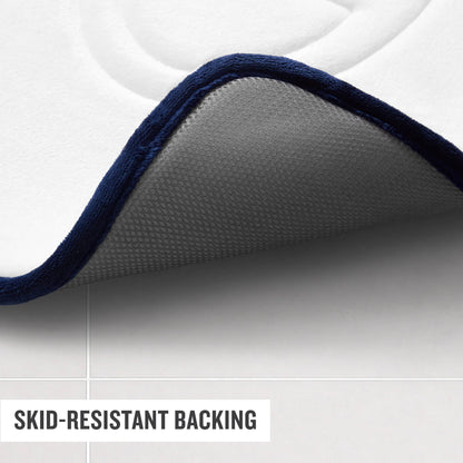 A close-up of the corner of a Champion Quilted Logo Memory Foam Bath Mat lifted up, revealing its textured, gray skid-resistant backing on a tile floor. The image also features text that reads SKID-RESISTANT BACKING.