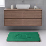 Modern bathroom with a floating wood vanity, white vessel sink, and a Champion Quilted Logo Memory Foam Bath Mat featuring a large embossed letter C on a light gray tiled floor.