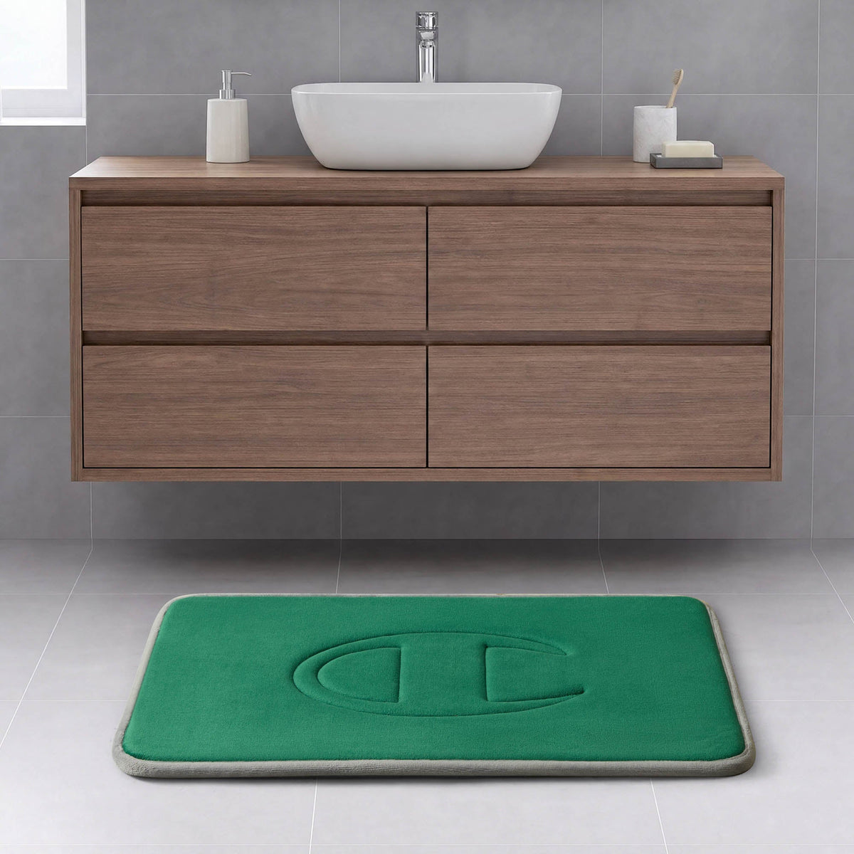 Modern bathroom with a floating wood vanity, white vessel sink, and a Champion Quilted Logo Memory Foam Bath Mat featuring a large embossed letter C on a light gray tiled floor.