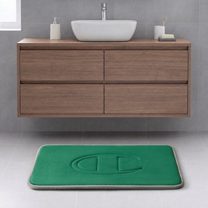 Modern bathroom with a floating wood vanity, white vessel sink, and a Champion Quilted Logo Memory Foam Bath Mat featuring a large embossed letter C on a light gray tiled floor.