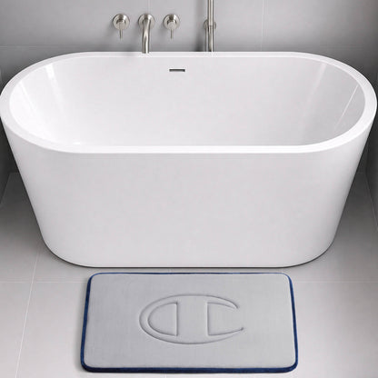 A modern white bathtub with wall-mounted faucets sits in a grey tiled bathroom. In front of the tub is a light grey Champion Quilted Logo Memory Foam Bath Mat, featuring a raised C logo, plush memory foam comfort, and a dark blue border.