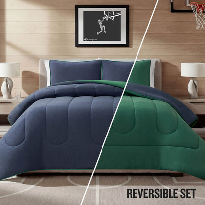 A neatly made bed features the Champion Premium Reversible Solid Jersey Comforter Set in blue and green, matching pillows, two bedside tables with lamps, and a framed basketball artwork above the headboard. The text “REVERSIBLE SET” appears at the bottom right.