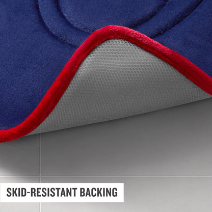 A close-up of a blue Champion Quilted Logo Memory Foam Bath Mat with a red edge, partially lifted to reveal its white, textured skid-resistant backing on a tiled floor. Text reads SKID-RESISTANT BACKING.
