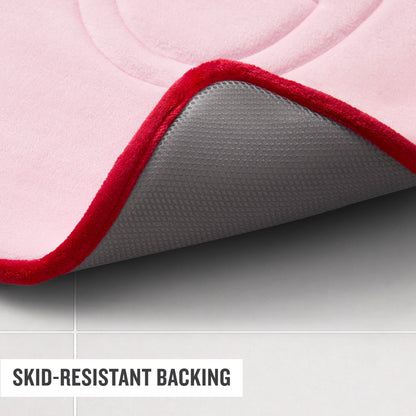 A close-up of the Champion Quilted Logo Memory Foam Bath Mat in pink with a red border, highlighting its gray skid-resistant backing, placed on a light tiled floor. Text reads SKID-RESISTANT BACKING.