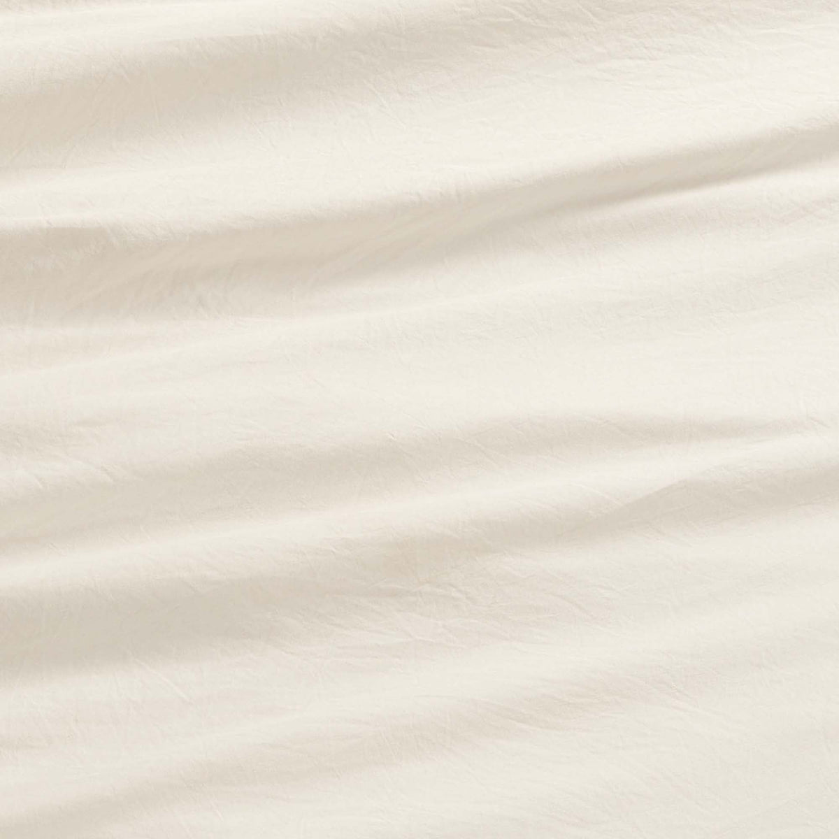 Close-up of the Champion Elastic Logo Microfiber Sheet Set in an off-white shade, showcasing gentle creases and a subtle textured surface. The lighting brings out the soft folds, highlighting the inviting and cozy feel of this everyday bedding essential.