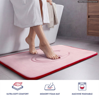A person steps onto a pink Champion Quilted Logo Memory Foam Bath Mat featuring plush memory foam in a bathroom. Icons below highlight features: ultra soft comfort, memory foam, and machine washable.