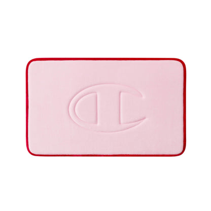 A rectangular pink Champion Quilted Logo Memory Foam Bath Mat with rounded corners and a red border, featuring an embossed large C-shaped logo in the center.