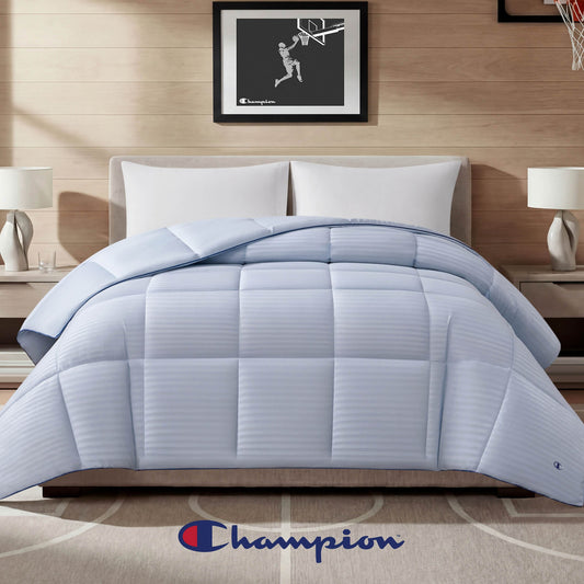A neatly made bed showcases the Champion Blue Cooling Down Alternative Comforter, complemented by two pillows, nightstands with lamps, and a distinctive Champion logo at the foot of the bed. Basketball-themed framed art hangs on the wall behind, completing this stylish setup featuring Champion bedding.