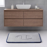 A modern bathroom with a floating wooden vanity, a vessel sink, and a rectangular gray Quilted Logo Memory Foam Bath Mat from Champion, featuring an embossed logo, set on a light tile floor.
