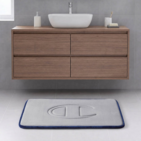 A modern bathroom with a floating wooden vanity, a vessel sink, and a rectangular gray Quilted Logo Memory Foam Bath Mat from Champion, featuring an embossed logo, set on a light tile floor.